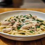 Chicken Alfredo served in a white bowl, garnished with parsley and Parmesan cheese.